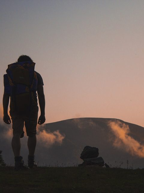 A hiker with a large pack walks a ridge at sunset