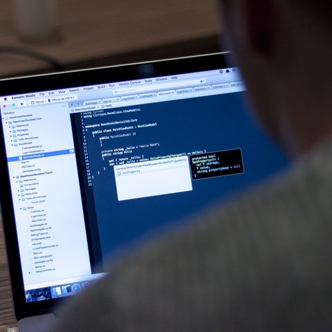 Developer seen from behind working on code in a laptop editor