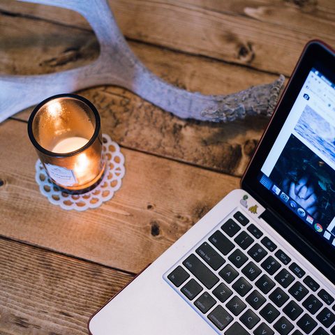 Laptop showing a photo gallery next to a lit candle on old wood