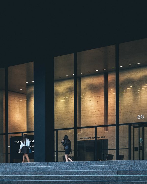Two people walking up the steps into a glass office building at dusk