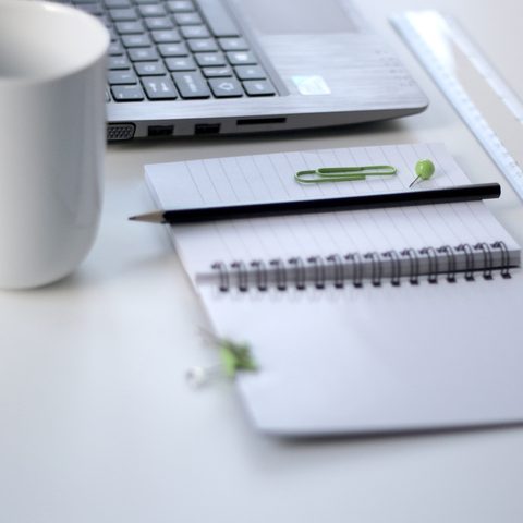 Open spiral notebook, ruler and white mug beside a laptop