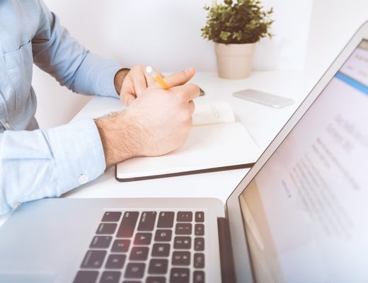 Hands writing notes next to an open laptop