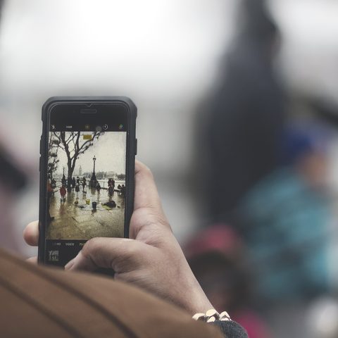 Hands holding a phone up to frame a busy street