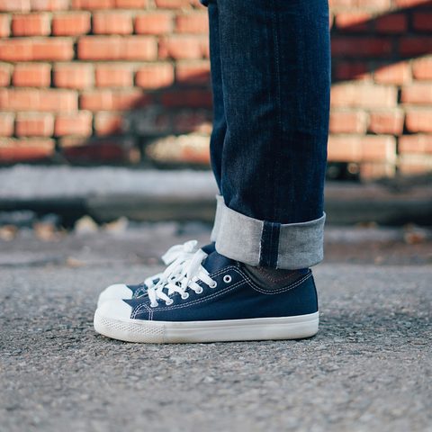 Navy canvas sneakers and rolled jeans on a street by a brick wall