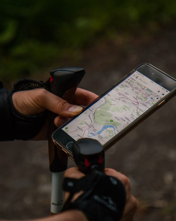 A walker with trekking poles checks a trail map on a phone