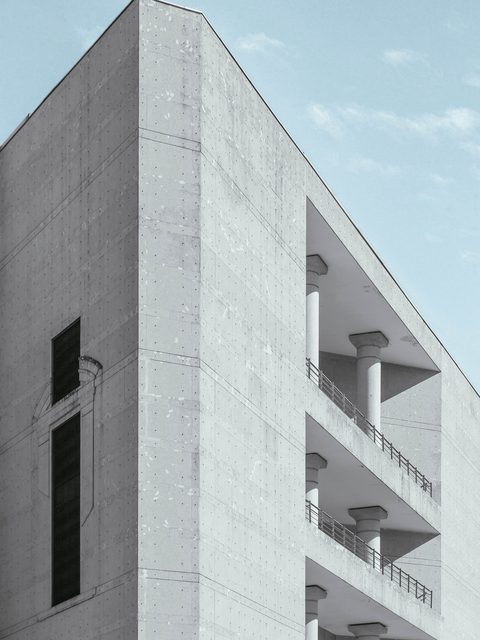 Corner of a pale concrete building with stacked balconies against blue sky