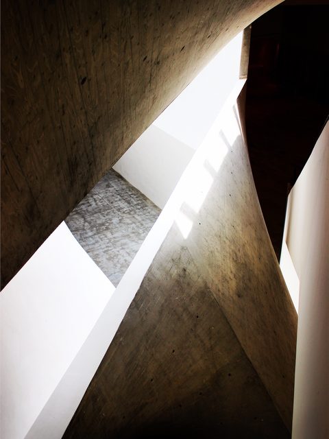 Daylight falling down a narrow shaft between angled concrete walls