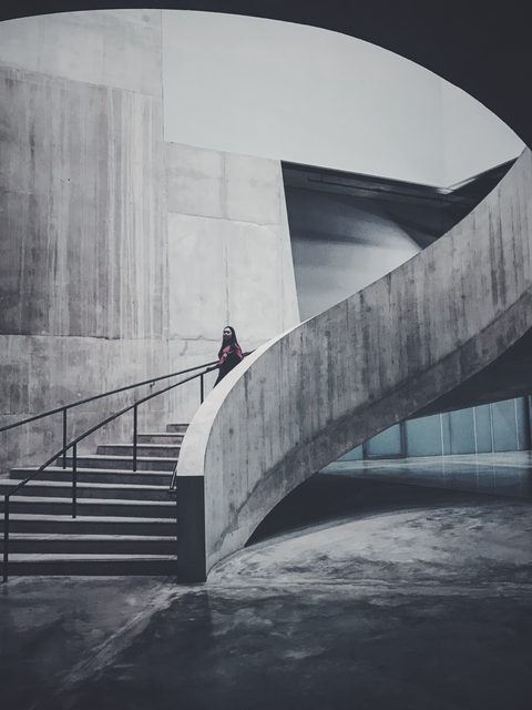 A curved concrete stair climbing past tall grey walls