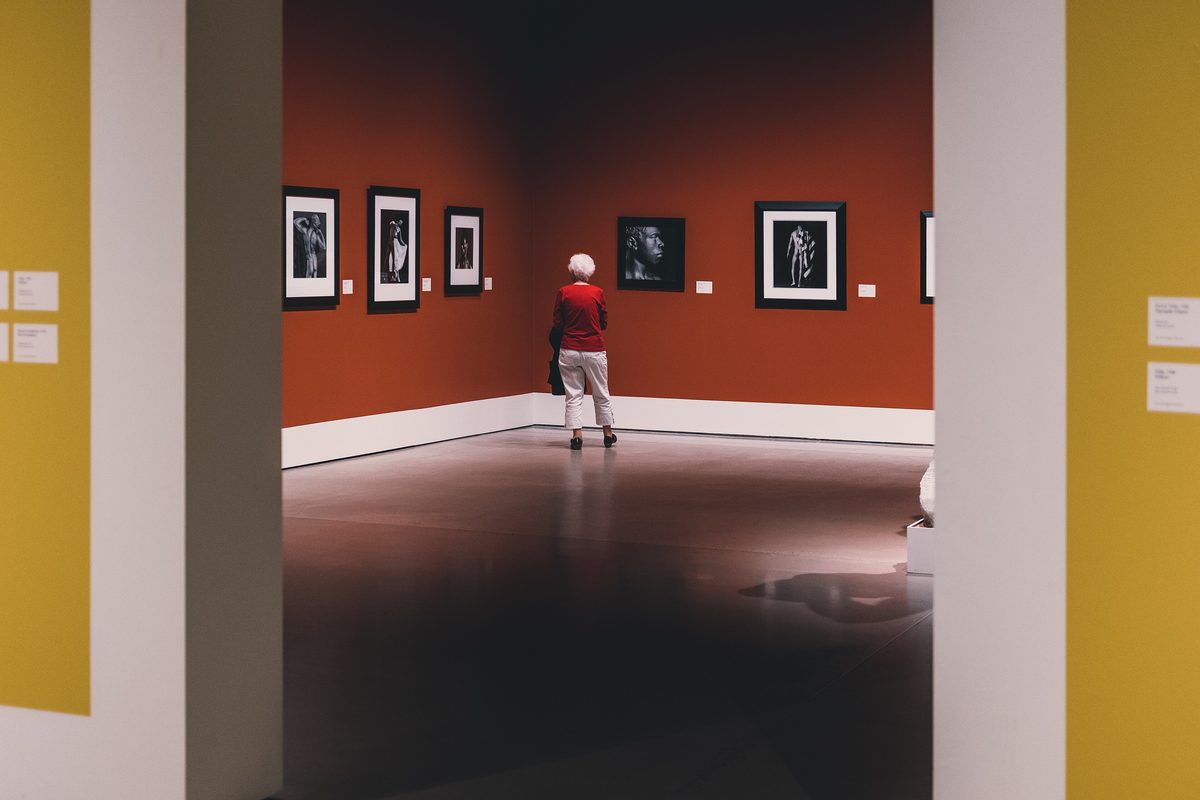 A visitor looking at black and white framed photographs on a deep red gallery wall