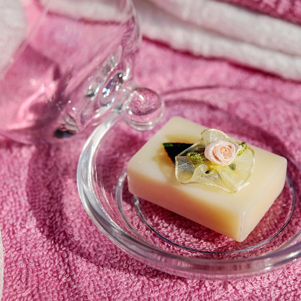 A cream soap bar with a tiny rose on a glass dish over a pink towel
