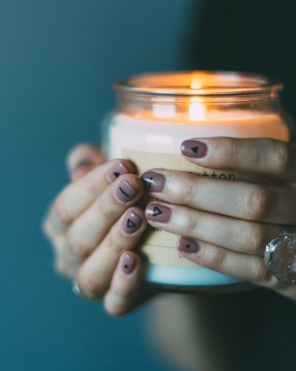 Hands with painted nails holding a lit candle in a glass jar