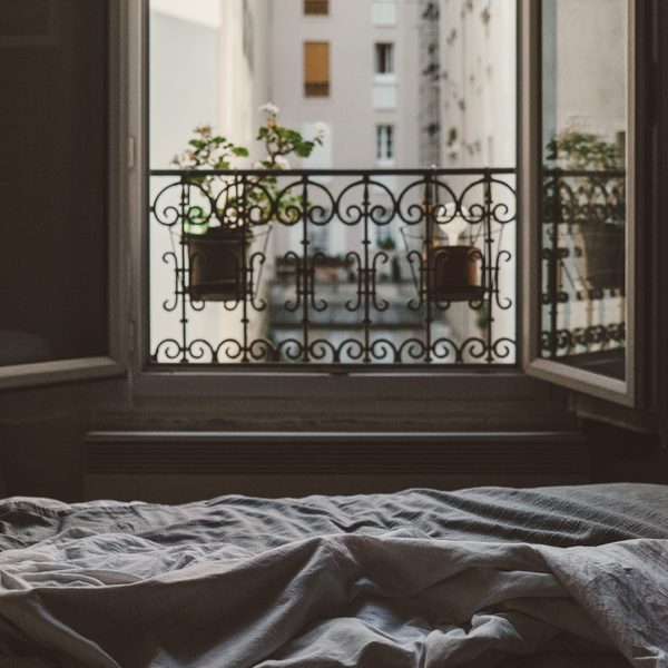 Rumpled grey bedding below an open window with iron railings