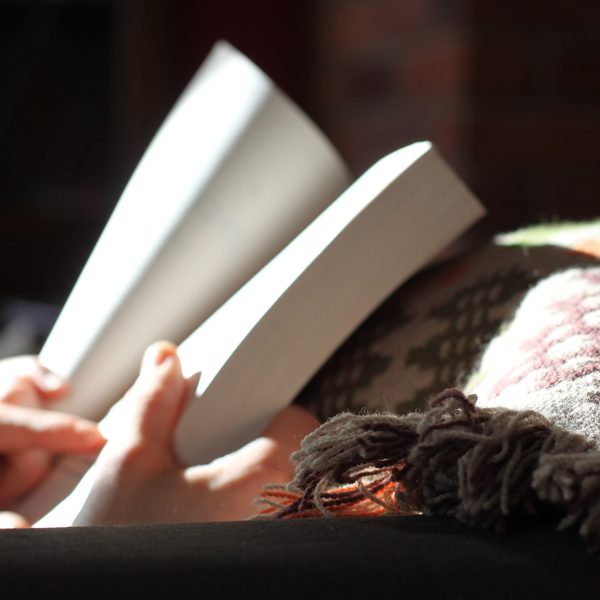 Hands holding an open book over a soft checked wool throw