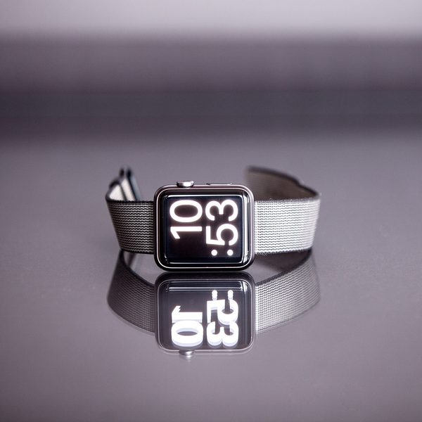 Smartwatch with a mesh strap standing on a glossy purple surface