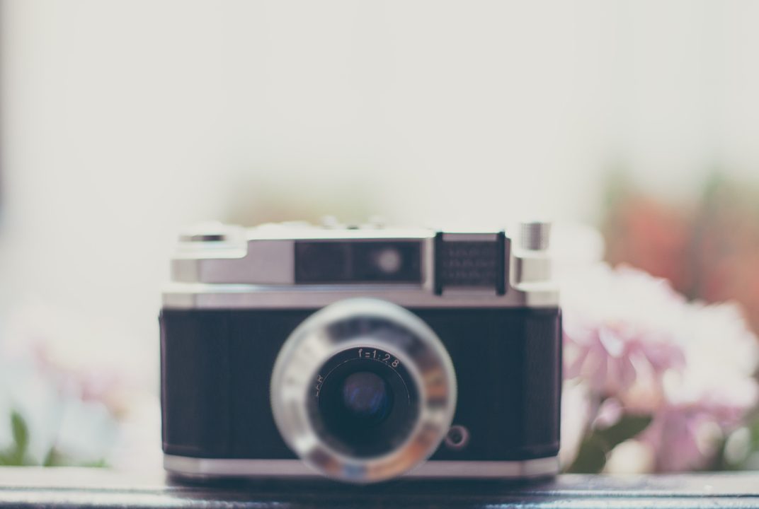 Silver rangefinder film camera on a window sill with pink flowers behind