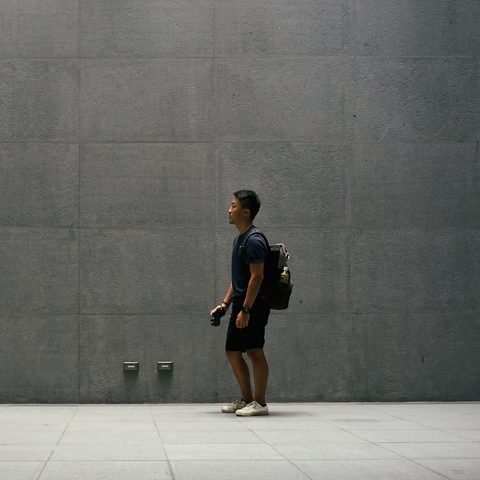 A student with a backpack seen from the side against a gray wall