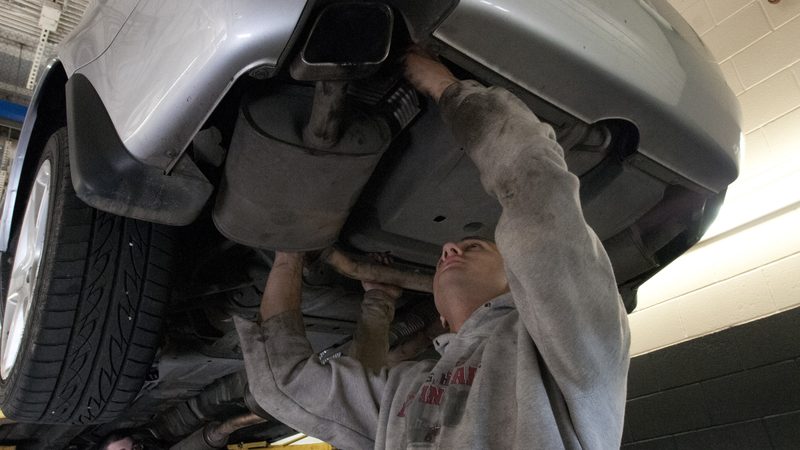 Mechanic working under a silver car raised on a lift