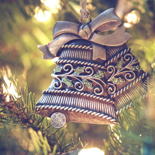 Silver bell ornament with a bow hanging on a pine branch