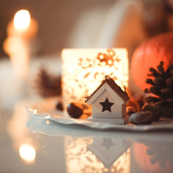 Glowing candle lantern with a small house and pine cones