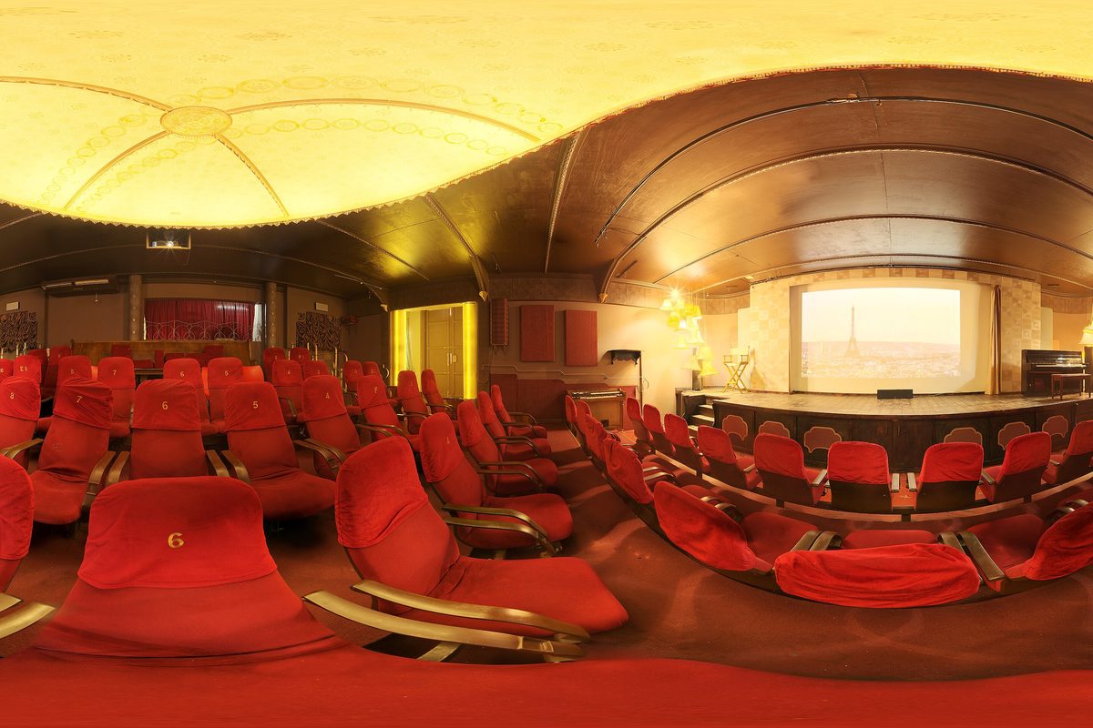 Rows of red velvet seats facing the screen in a warmly lit cinema hall