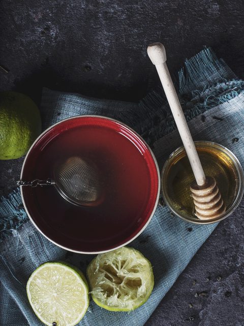A cup of herbal tea with honey and lime halves on a cloth