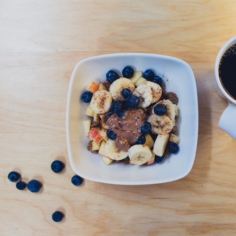 A bowl of oats with banana and blueberries next to a cup of black coffee