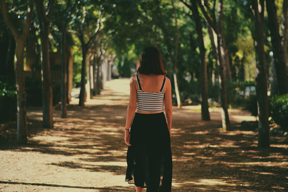 A woman walking away down a sunny path lined with trees