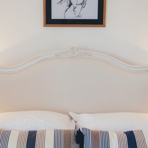 A made bed with striped pillows under a small framed horse drawing