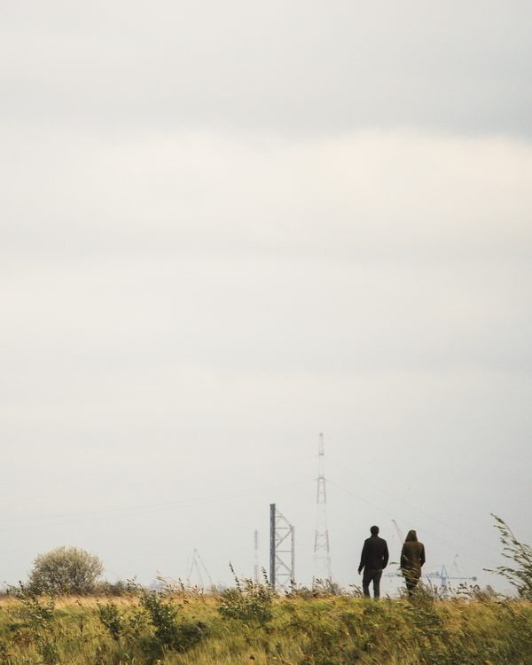 Two people walking side by side across a grassy field under a pale sky