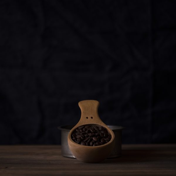 A wooden scoop of dark roasted beans on a dark table
