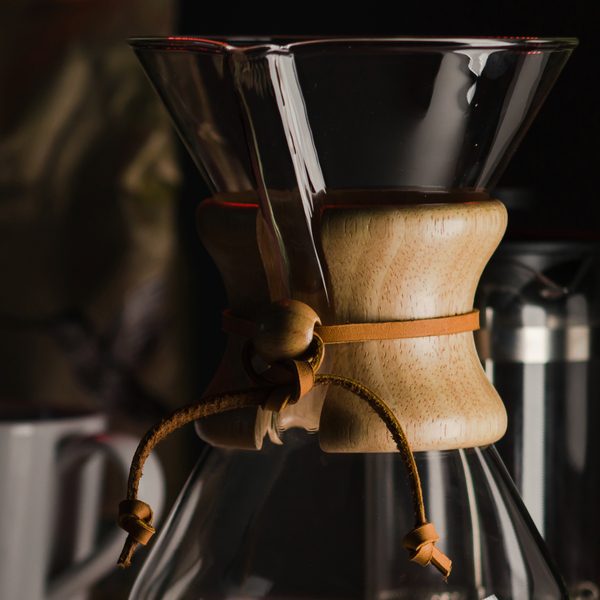 A glass pour over carafe with a wooden collar in low light