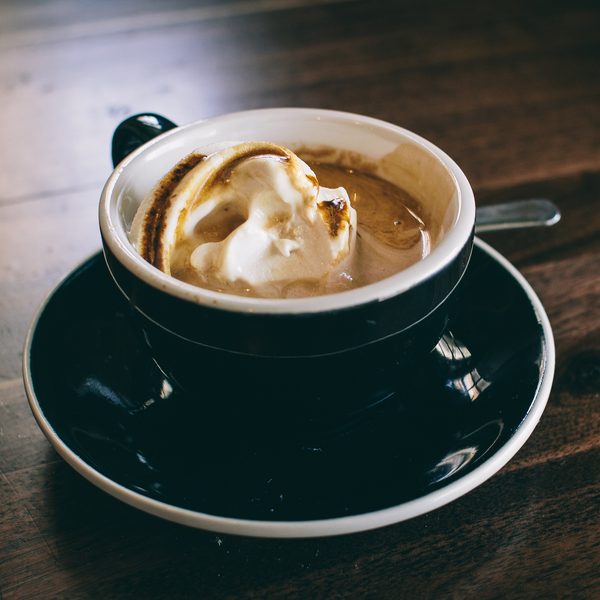 A cup of foamy coffee on a black saucer on a dark wooden table