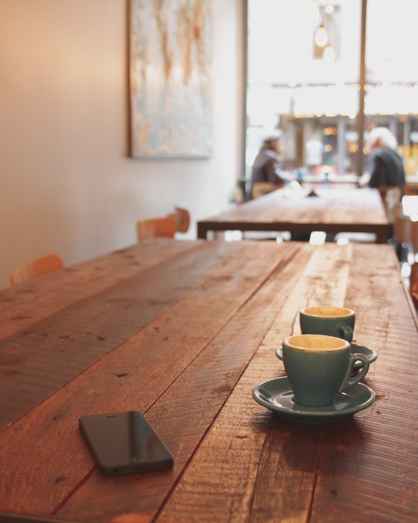 A cup of coffee on a long wooden table in a sunny cafe