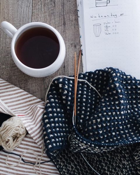 A half knitted navy cowl beside a cup of black coffee