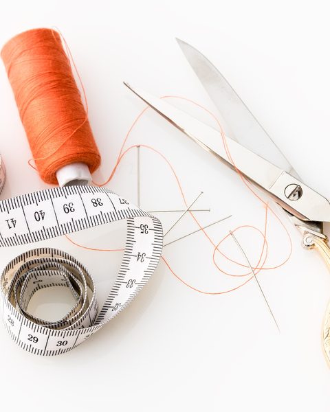 Orange thread, a tape measure and gold scissors on white