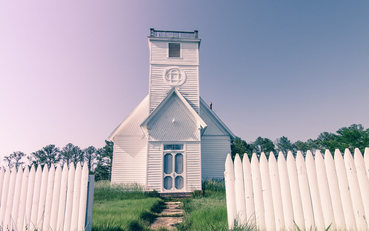 Small white country church with a bell tower behind a picket fence