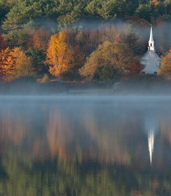 White church across a misty lake with autumn trees