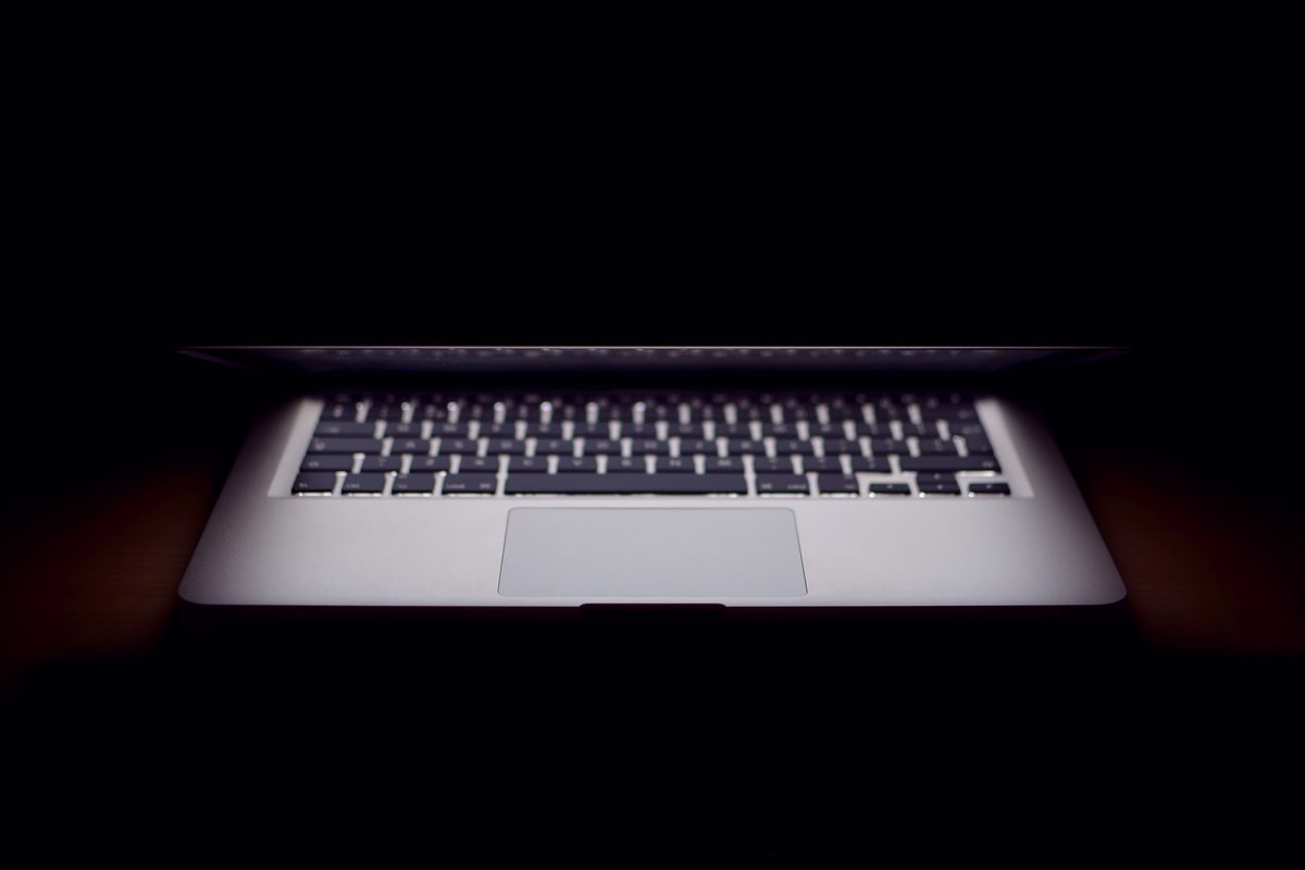 A half open laptop glowing in a dark room with its keyboard lit
