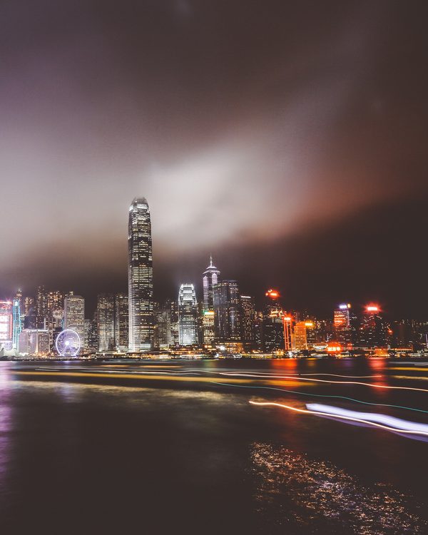 A lit city skyline under low clouds at night across dark water