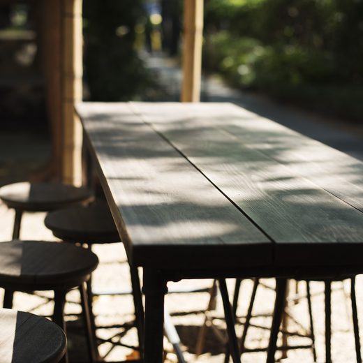 Long dark wooden table with round stools in a garden