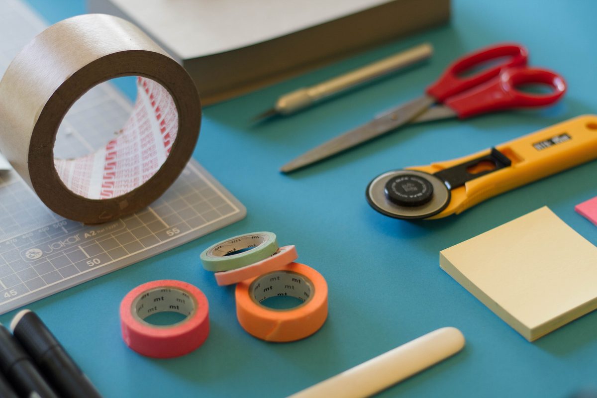 Tape, scissors, a rotary cutter and sticky notes on a teal work table