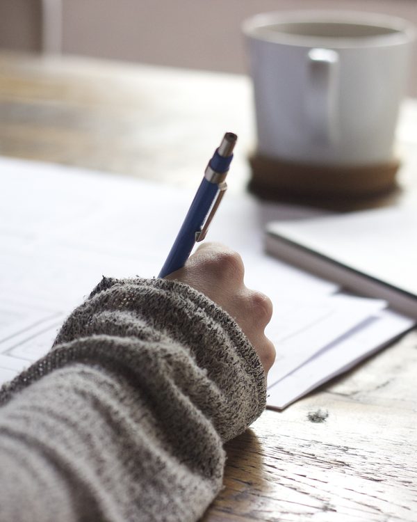 A hand in a knit sleeve sketches wireframes next to a coffee mug