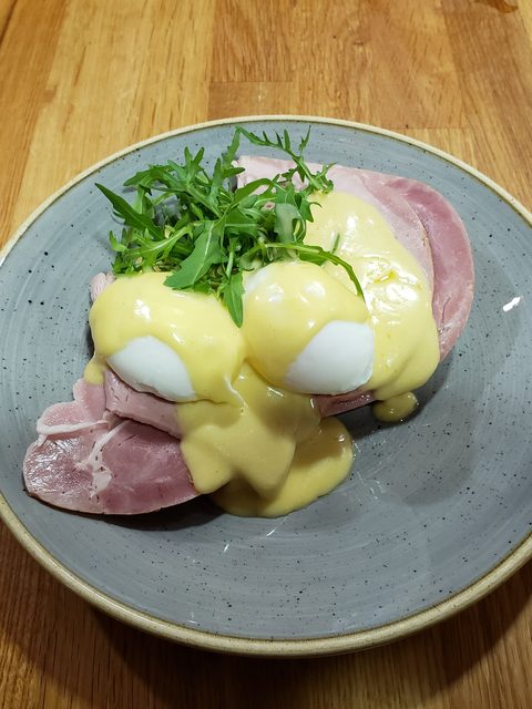 Eggs Benedict with ham, hollandaise and rocket on a grey plate