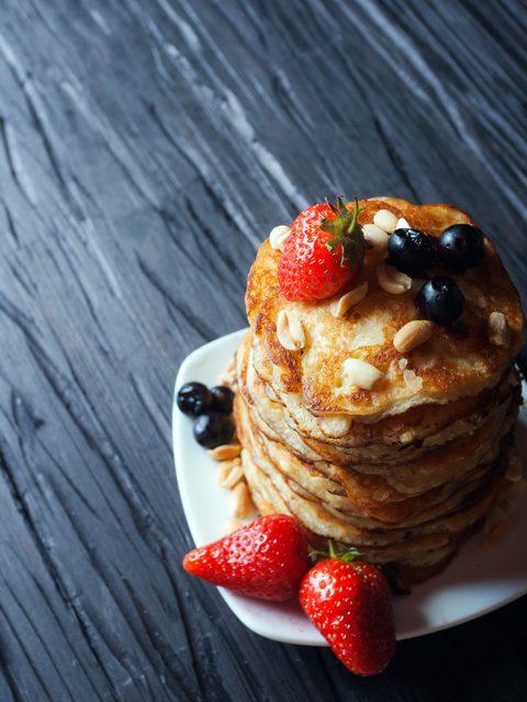 A stack of pancakes topped with strawberries, blueberries and syrup