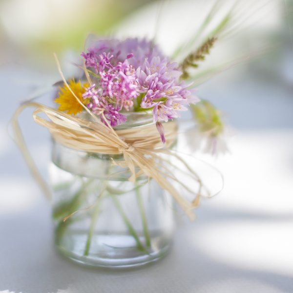 Purple wildflowers tied with raffia in a small glass jar