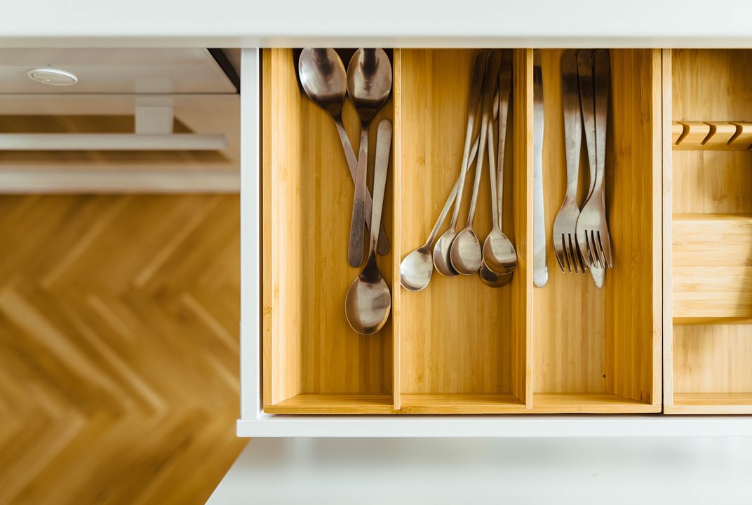 Open oak drawer with wood dividers holding spoons and forks