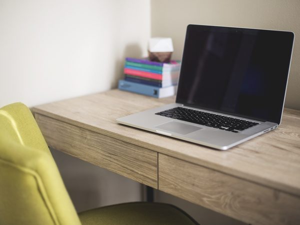 An open laptop on a light wooden desk beside a yellow chair