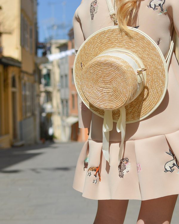Blush embroidered dress and a woven straw hat on a sunny old town street