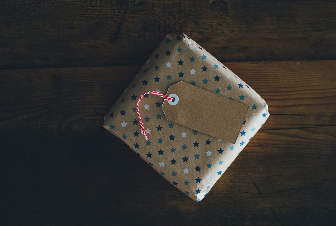 Gift wrapped in star print paper with red and white string and a kraft tag on dark wood