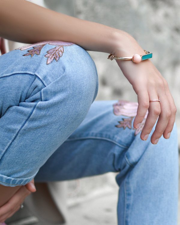 Light blue jeans with pink flower embroidery and a thin gold bracelet